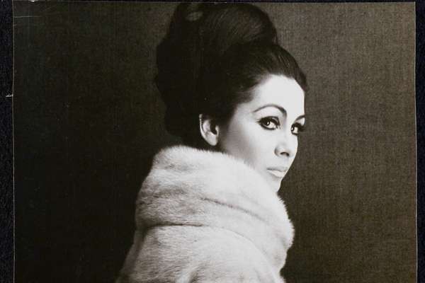 A black and white photo of a woman in a fur coat looking over her shoulder at the viewer.
