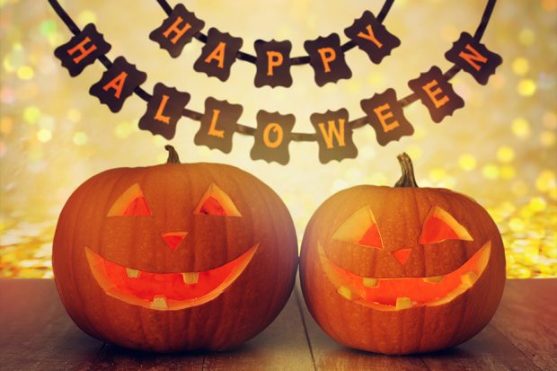 Two lit up pumpkins with a banner that reads happy halloween in the background