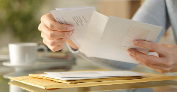 White woman's hands opening a white envelope.