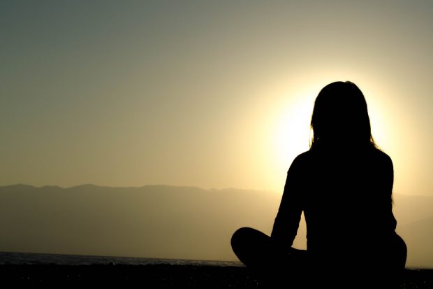 Photo of sunset with rear-view silhouette of woman sitting cross-legged in bottom right corner