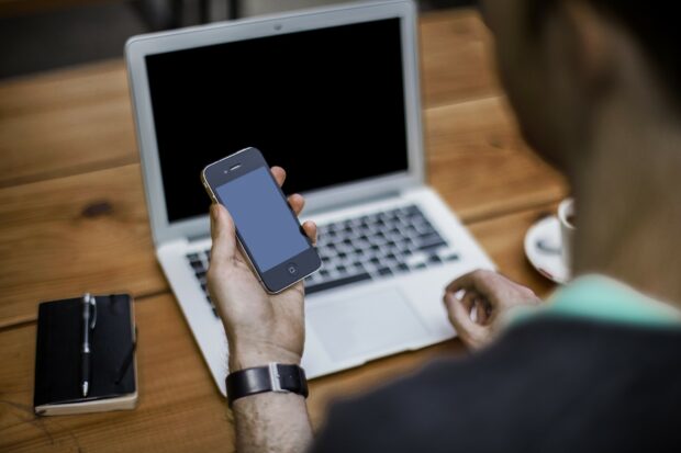 Person holding smartphone and looking at laptop screen