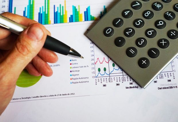Hand holding pen, paper containing graphs and a calculator
