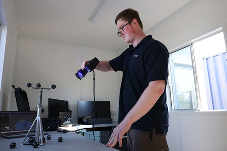 Man holding a small device in front of him scanning small items on a table.