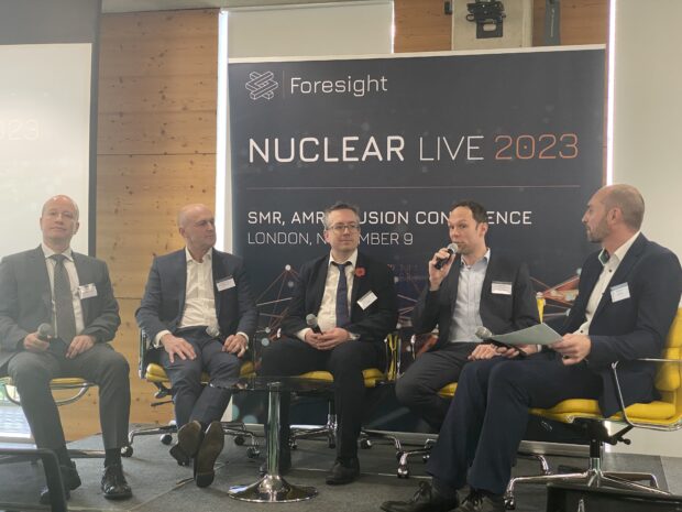 A panel of five conference attendees, including presenters, are gathered on a stage, holding a question and answer session with the audience.