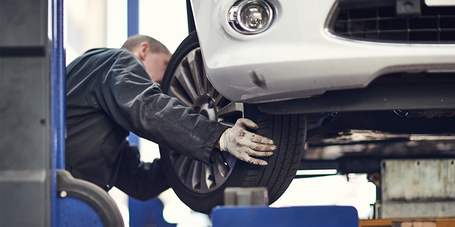 An MOT tester looks at a tyre on a car, in a garage.