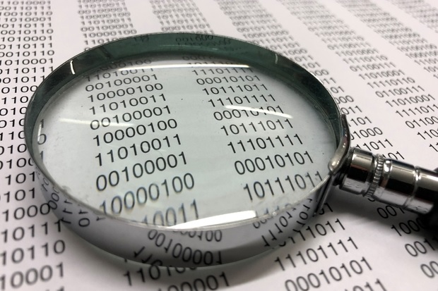 Page of binary code with a magnifying glass laying on the page.