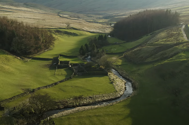 Arial view of Orton Fells. A beck wiggles through green hilly landscape