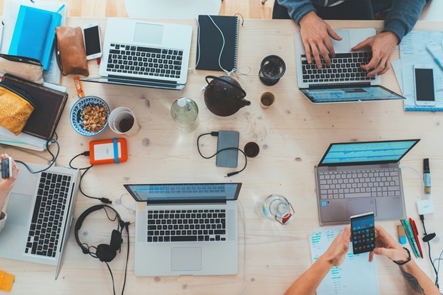A group of people sitting around a table with laptops