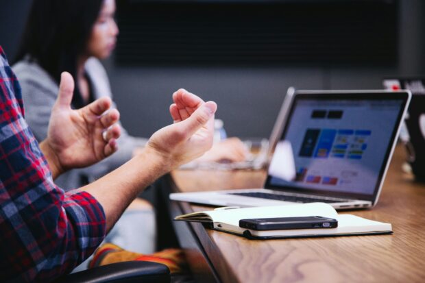A pair of hands is shown in the foreground and a laptop on a desk in the background.