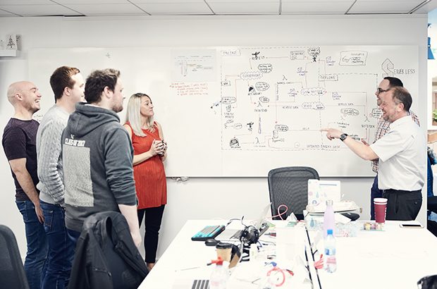 DVSA digital team staff gathering round a whiteboard with text on it