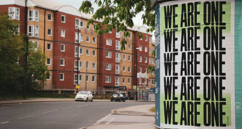 A photograph of a street of flats with a banner saying "we are one", highlighting the importance of people and place in local communities