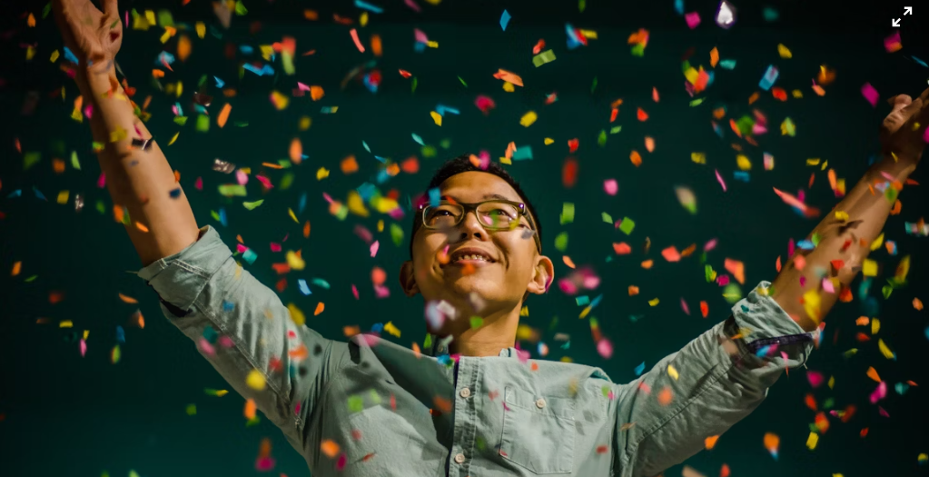 person with their arms raised with confetti raining down around them