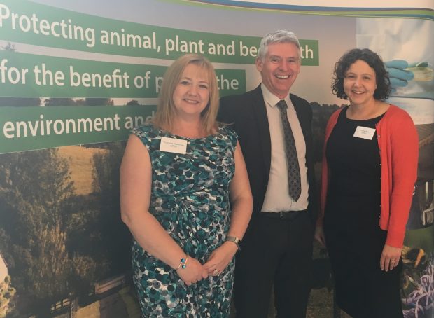 Two female and one male APHA Heads of Department posing for a photograph together in front of an APHA banner saying 'promoting animal, plant and bee health'
