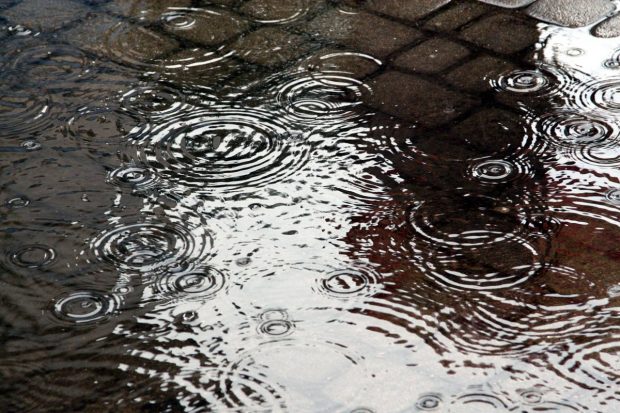 Close up photo showing raindrops landing in water on a flooded pavement