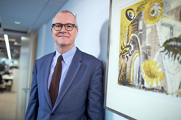 Photograph of Dr Patrick Vallance, Government Chief Scientific Adviser, in a blue suit standing by a wall next to a framed print of an abstract painting with sunflowers