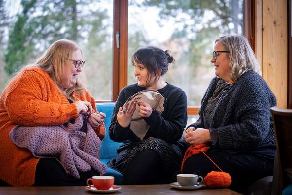 Three women sit on a sofa with sewing and yarn