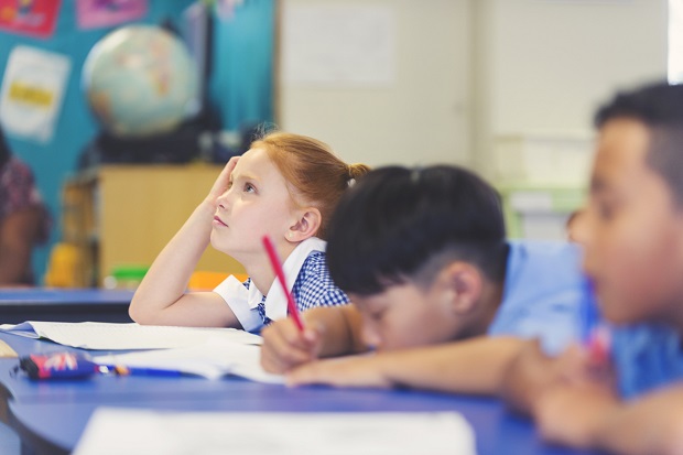 Three Children sat next to each other, looking ahead in a classroom.