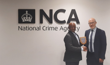 Two men in front of the NCA logo