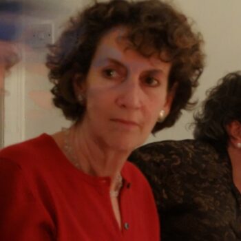 Photograph of a portrait of a person with short curly hair and wearing a red cardigan