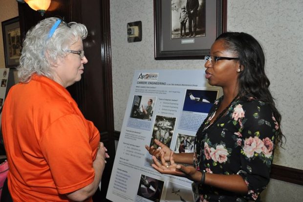 The image shows two ladies where one is describing the contents of a board which has some writing on it.