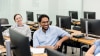 A group of students engaged in a training session, using computers in a bright classroom setting.