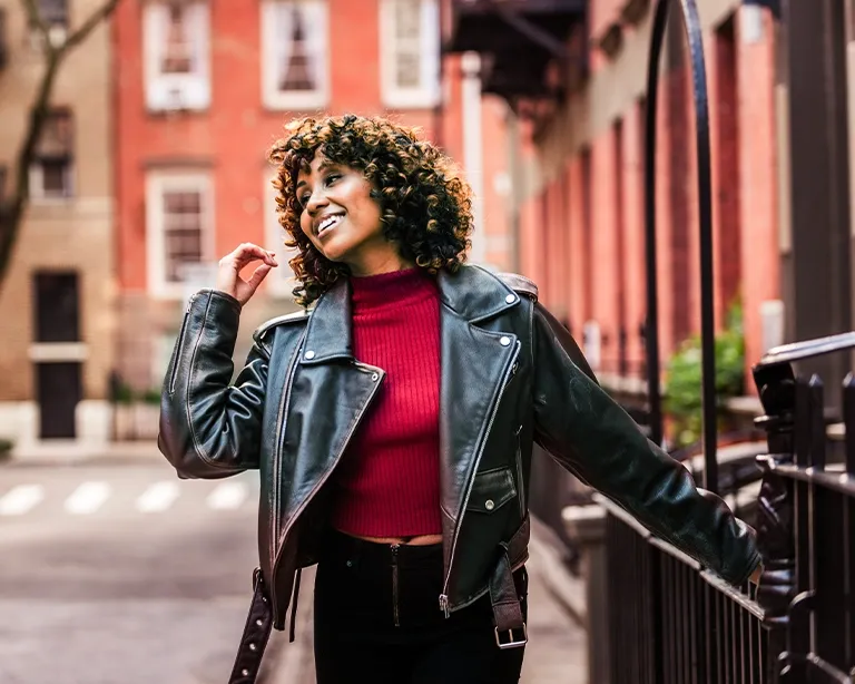 Curly-haired young woman smiling while walking through a European city street.