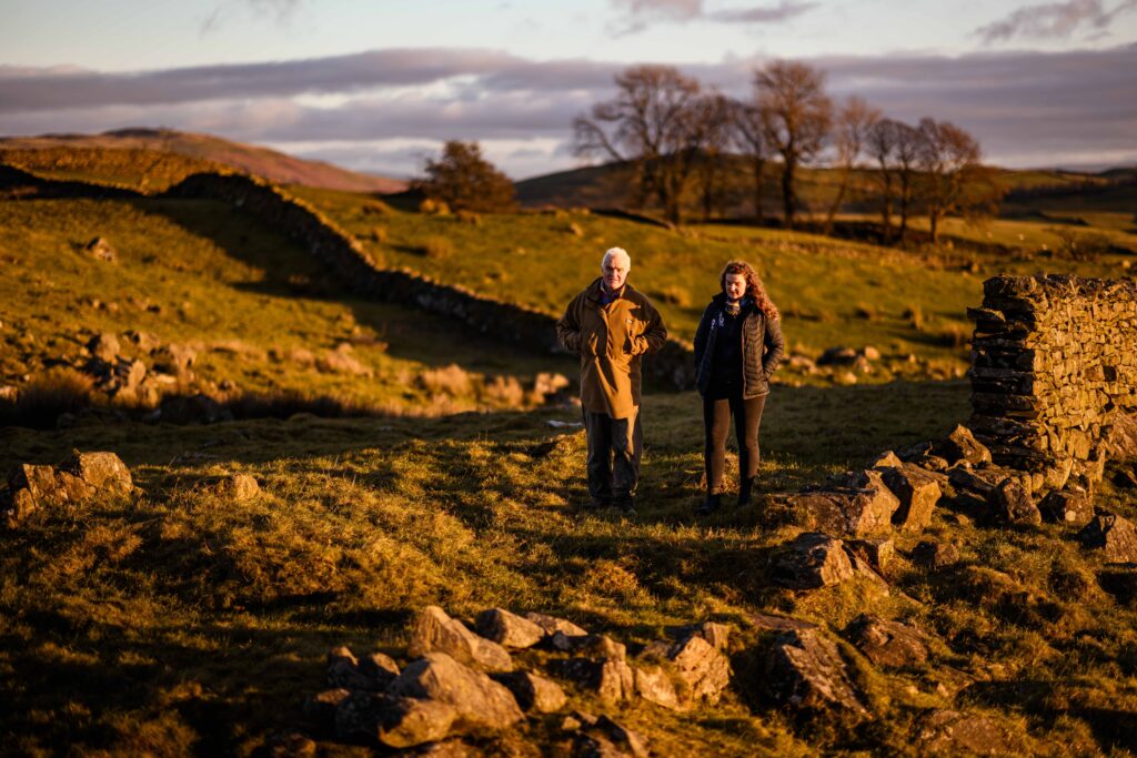 farming officer and farmer walking across field with dry stone walls in the orange evening sunlight