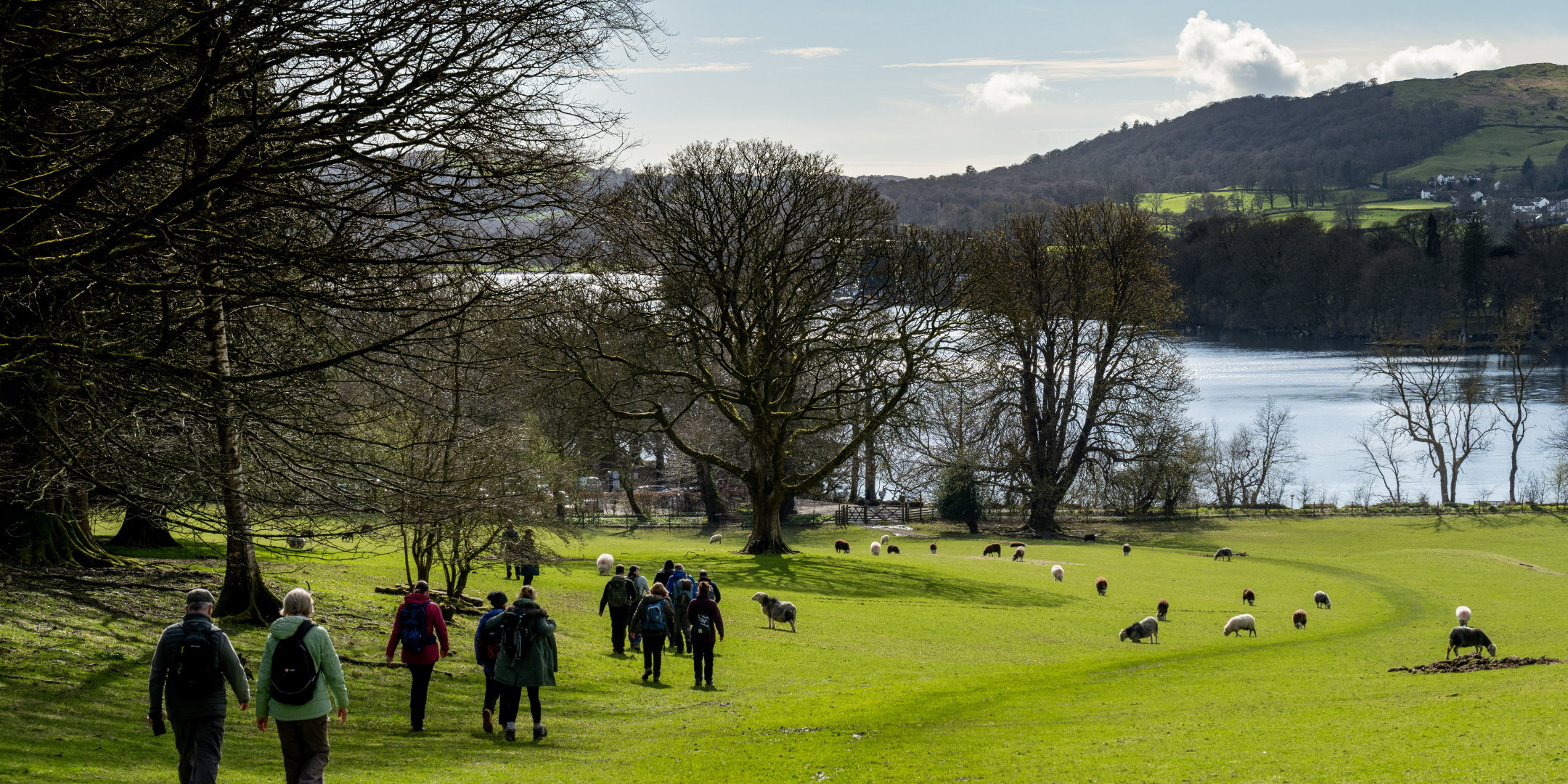 group of walkers in a field with sheet, surrounded by woodland with a lake and low hills in the backdrop