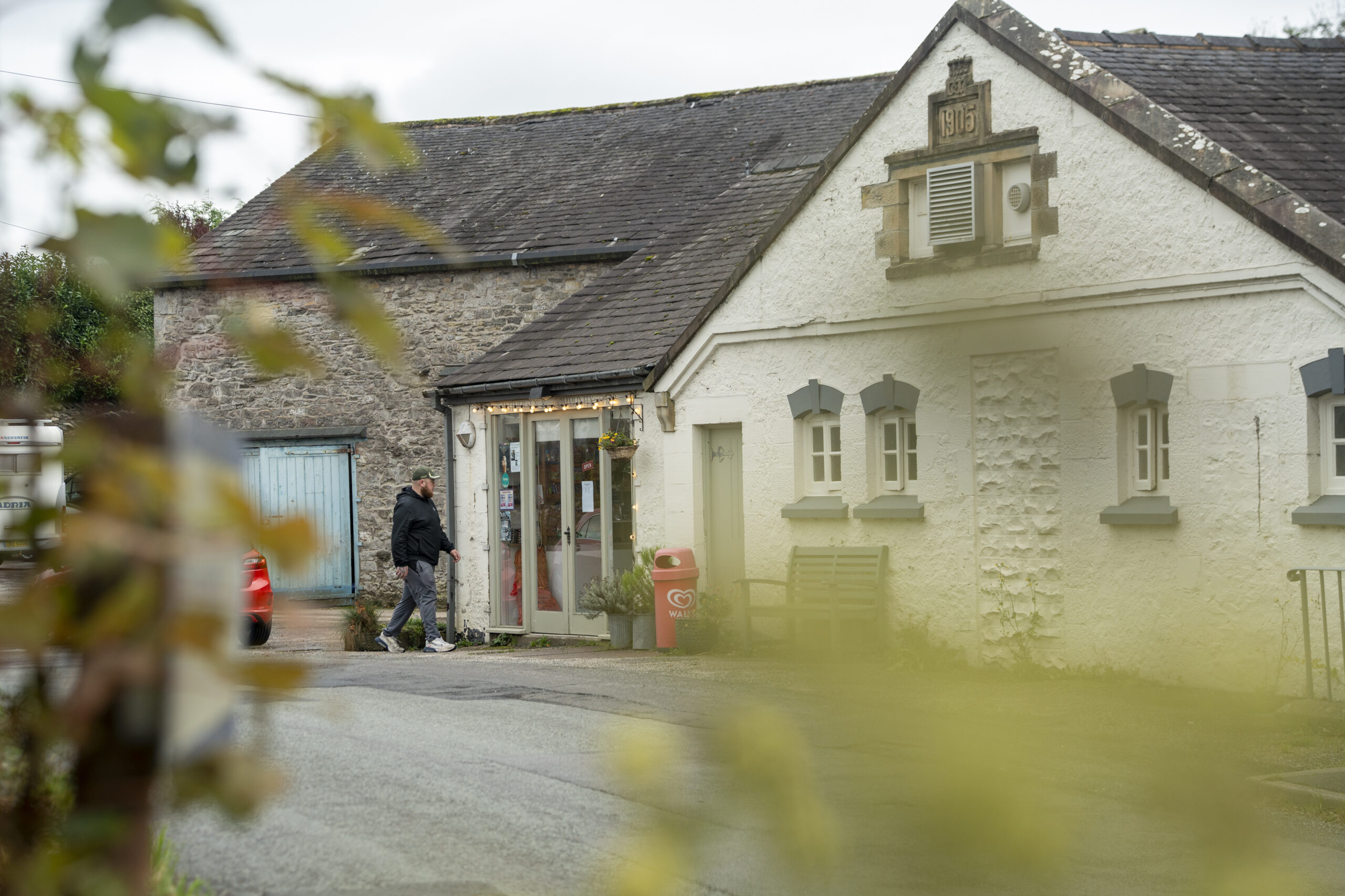 cream painted brick and stone local shop with an adult male walking in the entrance