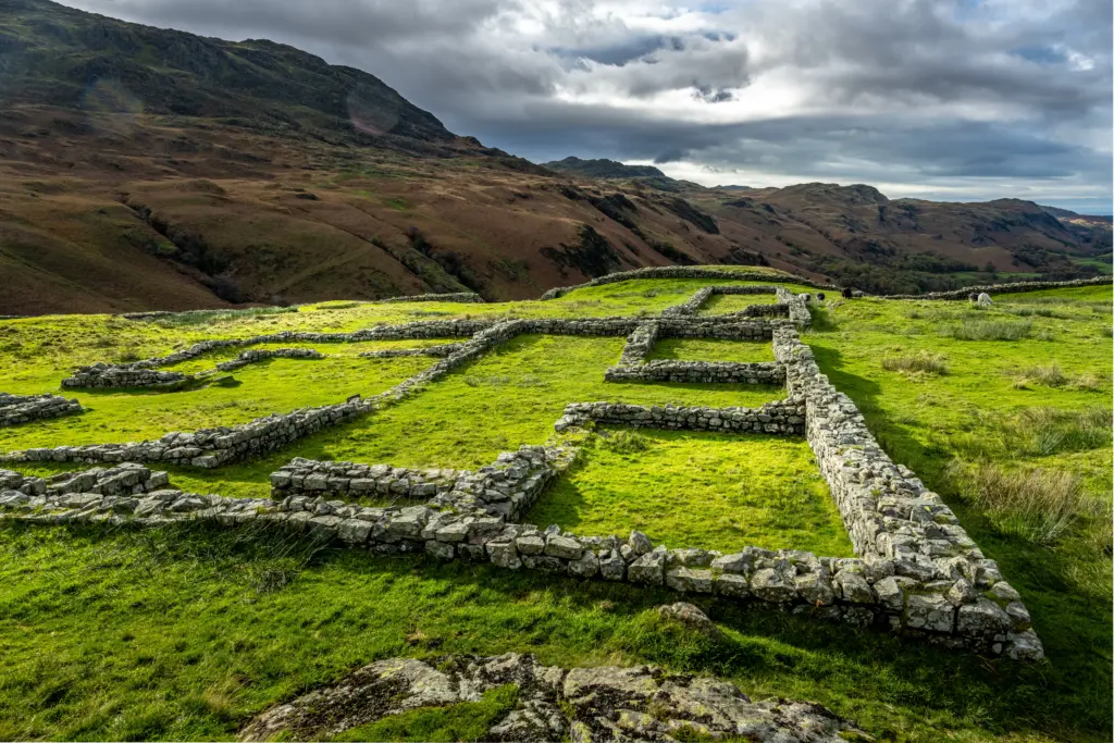 Arial view of Hardknott Roman fort stone remains on a green field, fell landscape in background