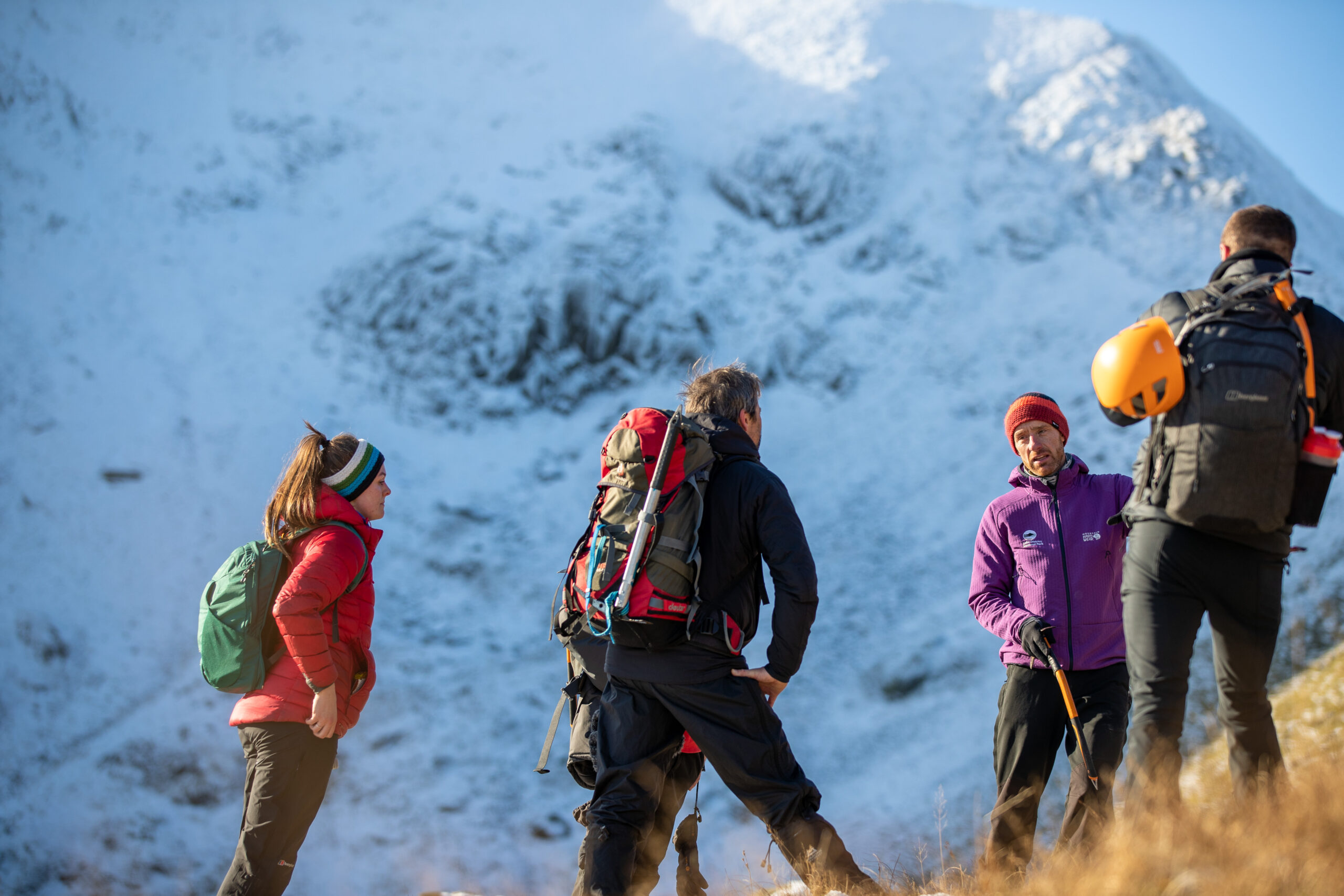 group of adults in winter outdoor clothing on fell slope with snow covered helvellyn in backdrop