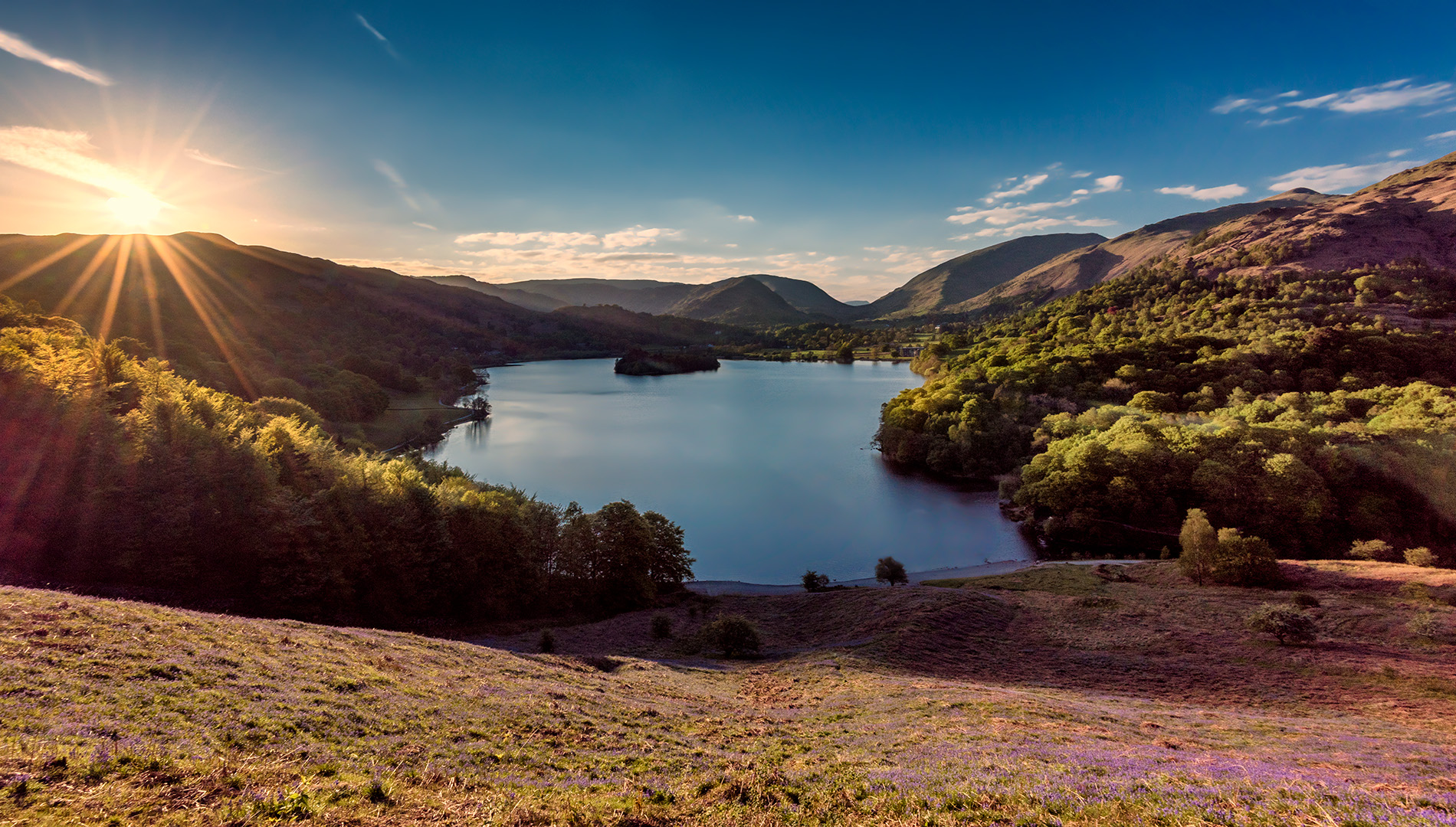 looking down onto Grasmere waterwith fells surrounding it and sun shining