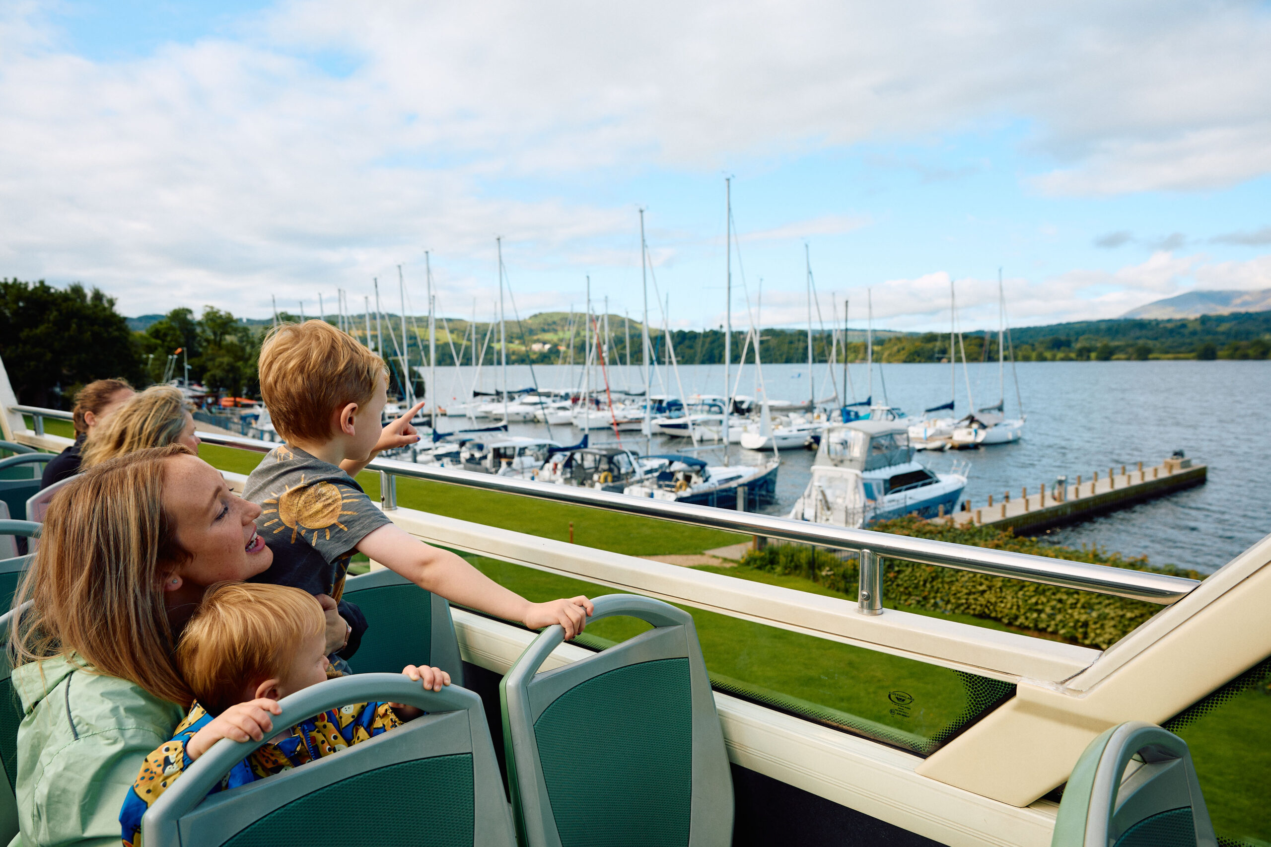 adult female and two young children sat on open top bus looking out to lake and moored boats