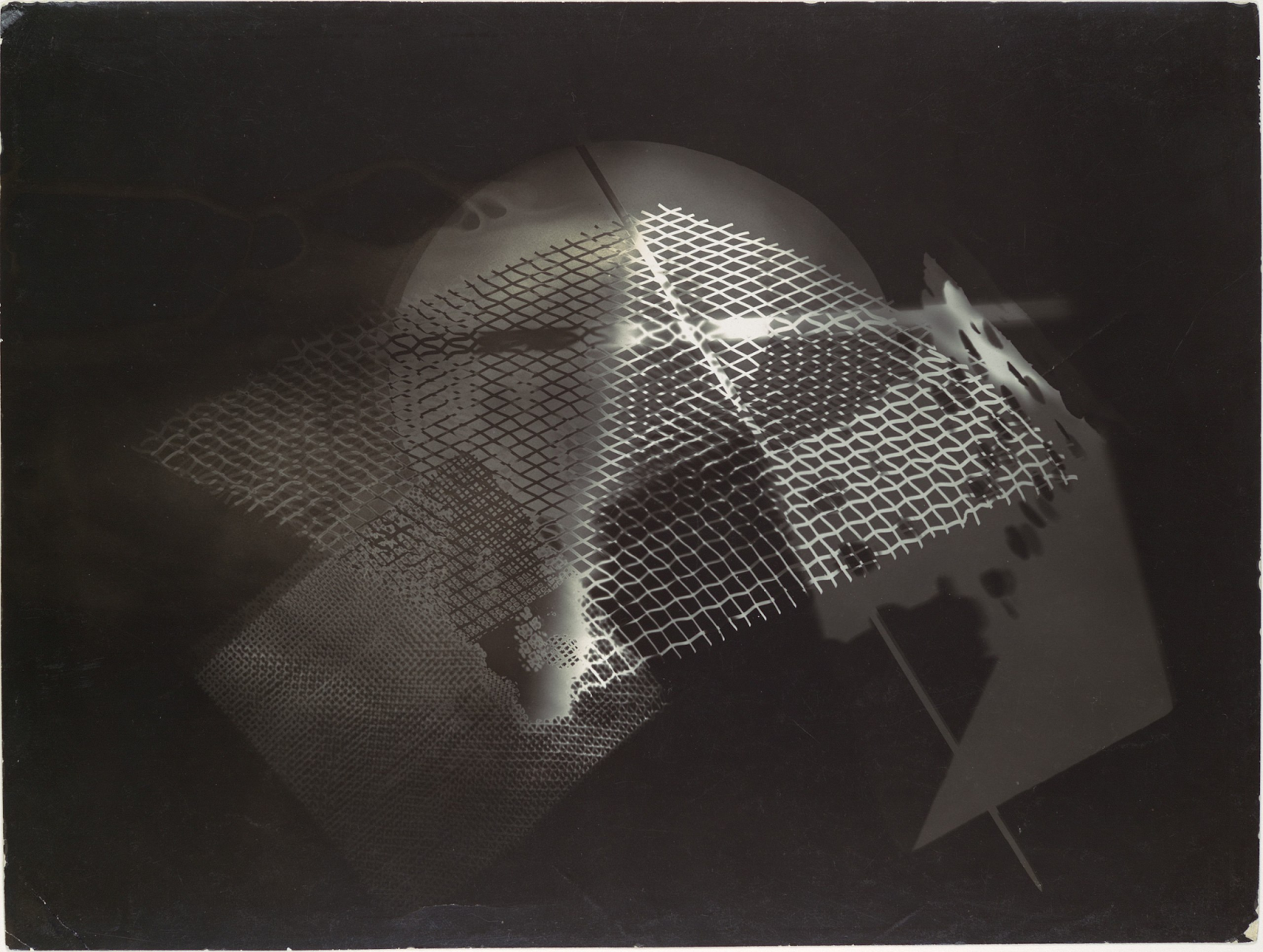 A photogram with abstract geometric patterns created by László Moholy-Nagy. The monochromatic composition features overlapping textures and shapes, including grids, lines, and amorphous forms, all captured through the direct exposure of objects on photographic paper. This experimental piece explores light, shadow, and transparency, showcasing Moholy-Nagy’s innovative approach to visual art and technology.