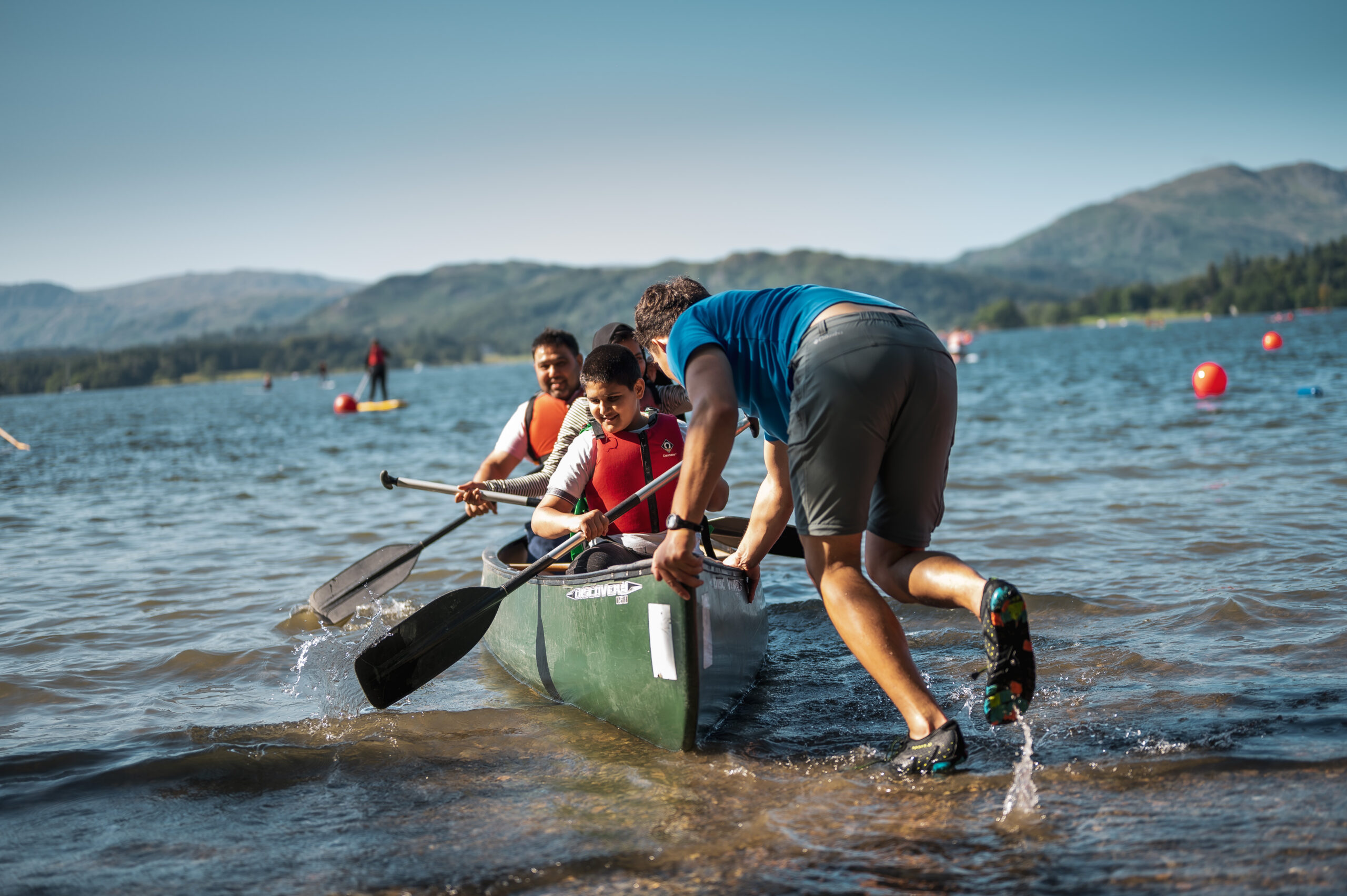adult male staff pushing two smiling kayakers out into coniston water