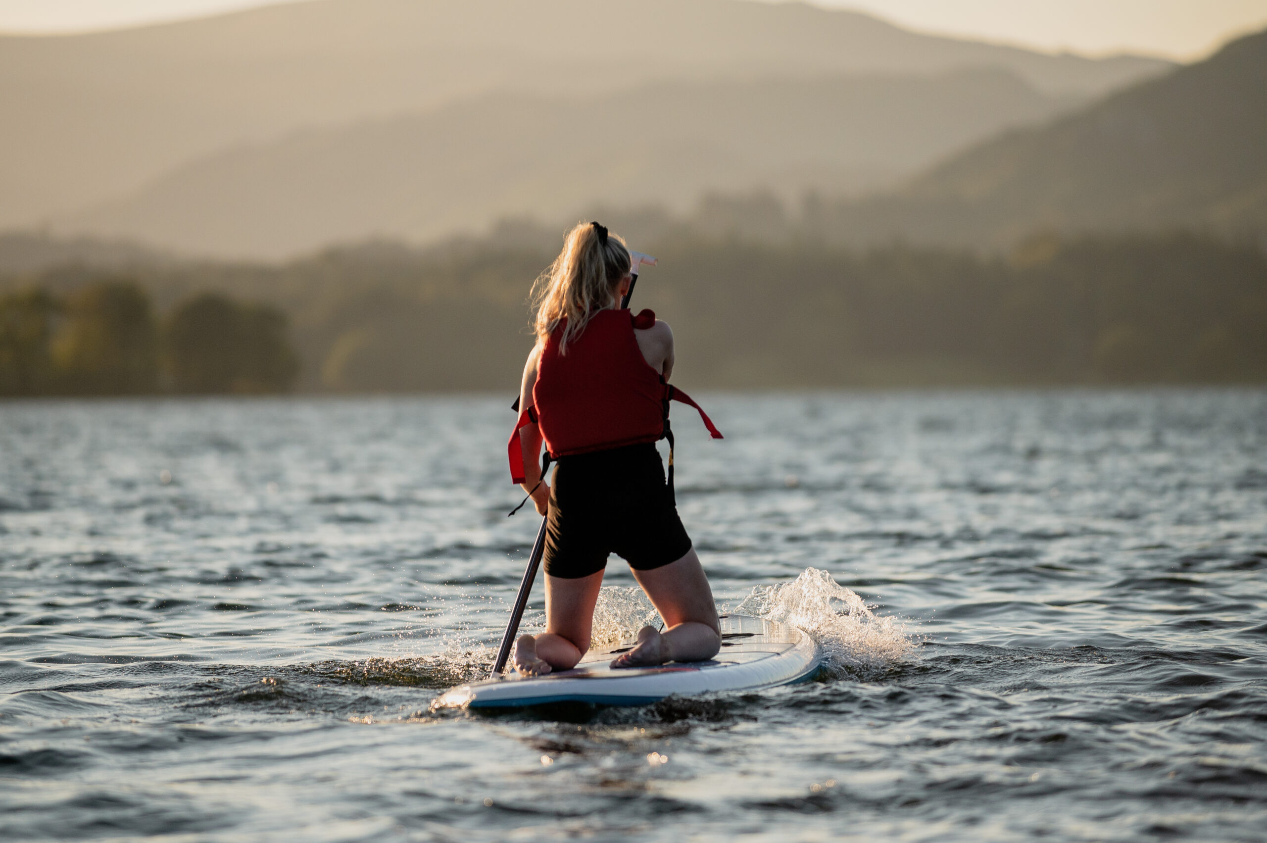 adult female kneeling on paddle board at sunset
