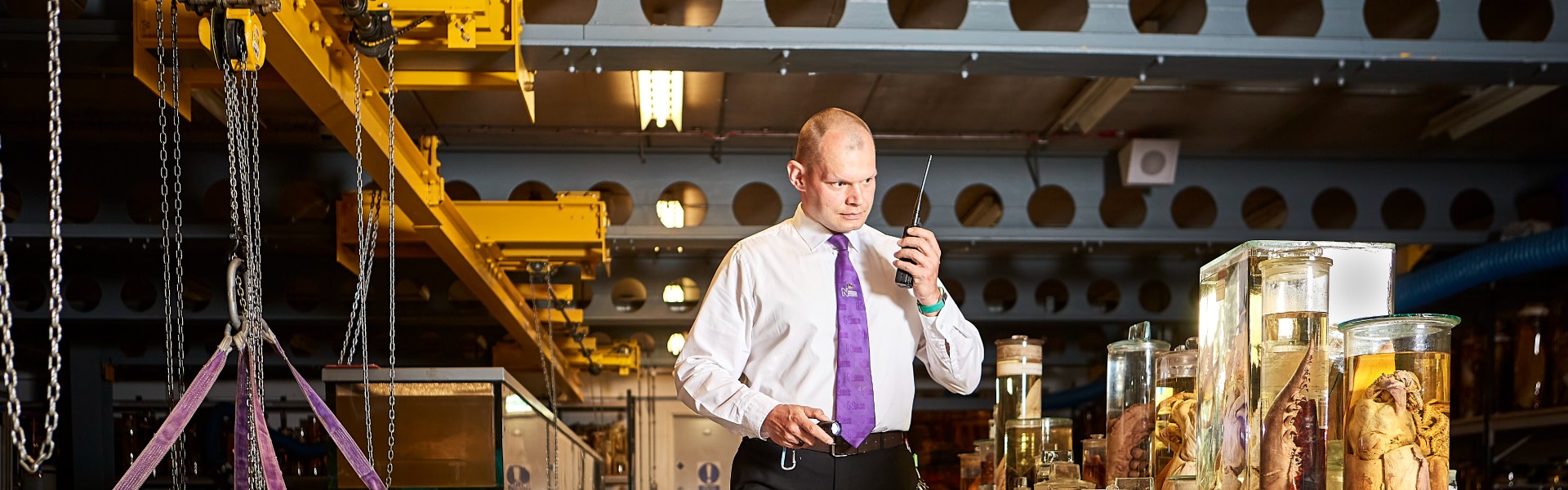 A security guard holding a torch and walkie-talkie while surrounded by specimens in the spirit collection.