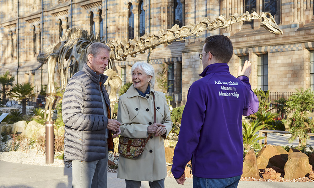A tour guide speaks to an elder couple in front of Fern the diplodocus at our gardens