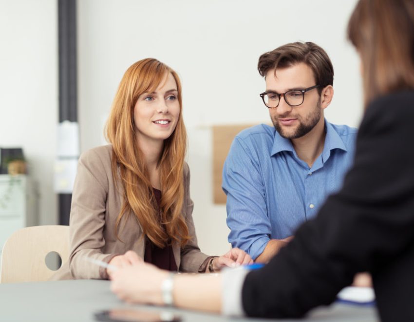 Man and woman sat at a desk talking to another woman