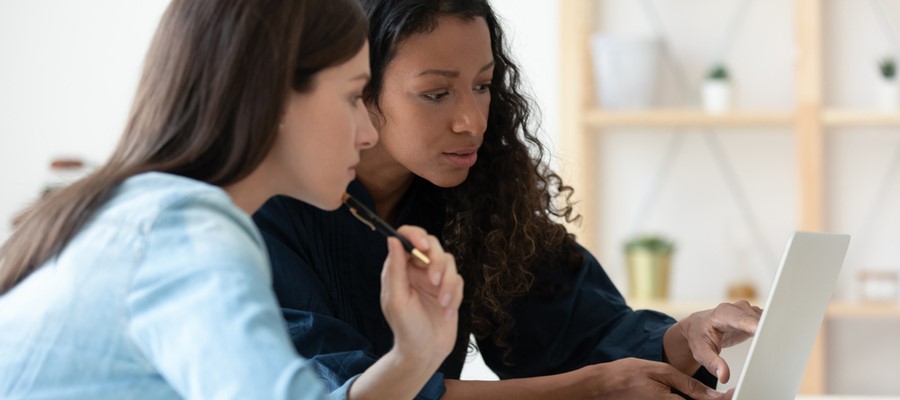 Two women pointing to and discussing a laptop screen