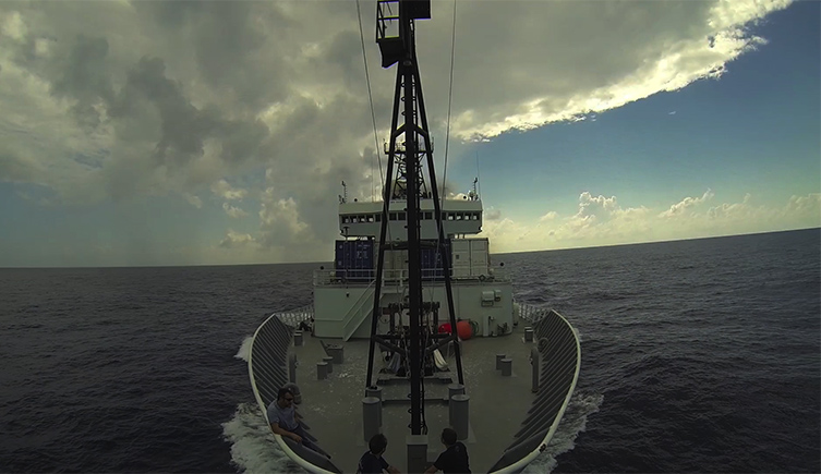 A boat on the ocean with the sky and clouds above