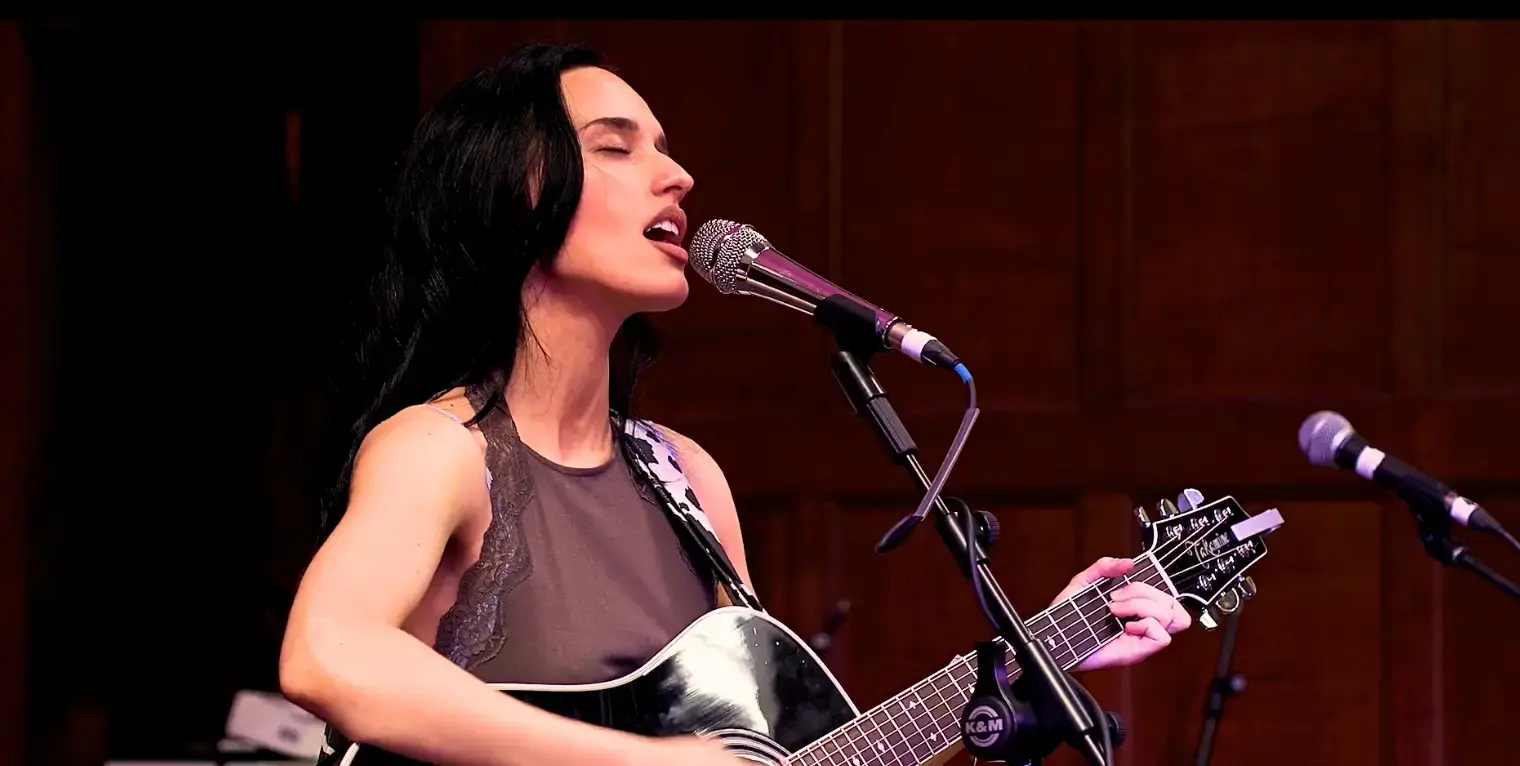 Lady playing electric guitar with eyes closed, singing into a microphone.