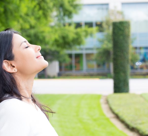 Woman in an office green space looking up while smiling with her eyes closed