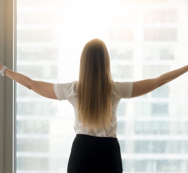 Back of a woman standing at a window with her arms out stretched