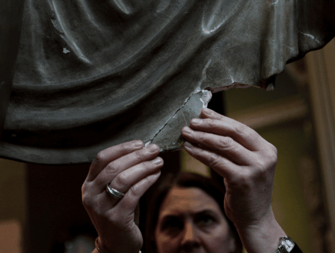 A conservator holds up a detached element of a plaster cast which has become divorced from its statue, to show where it should be restored.