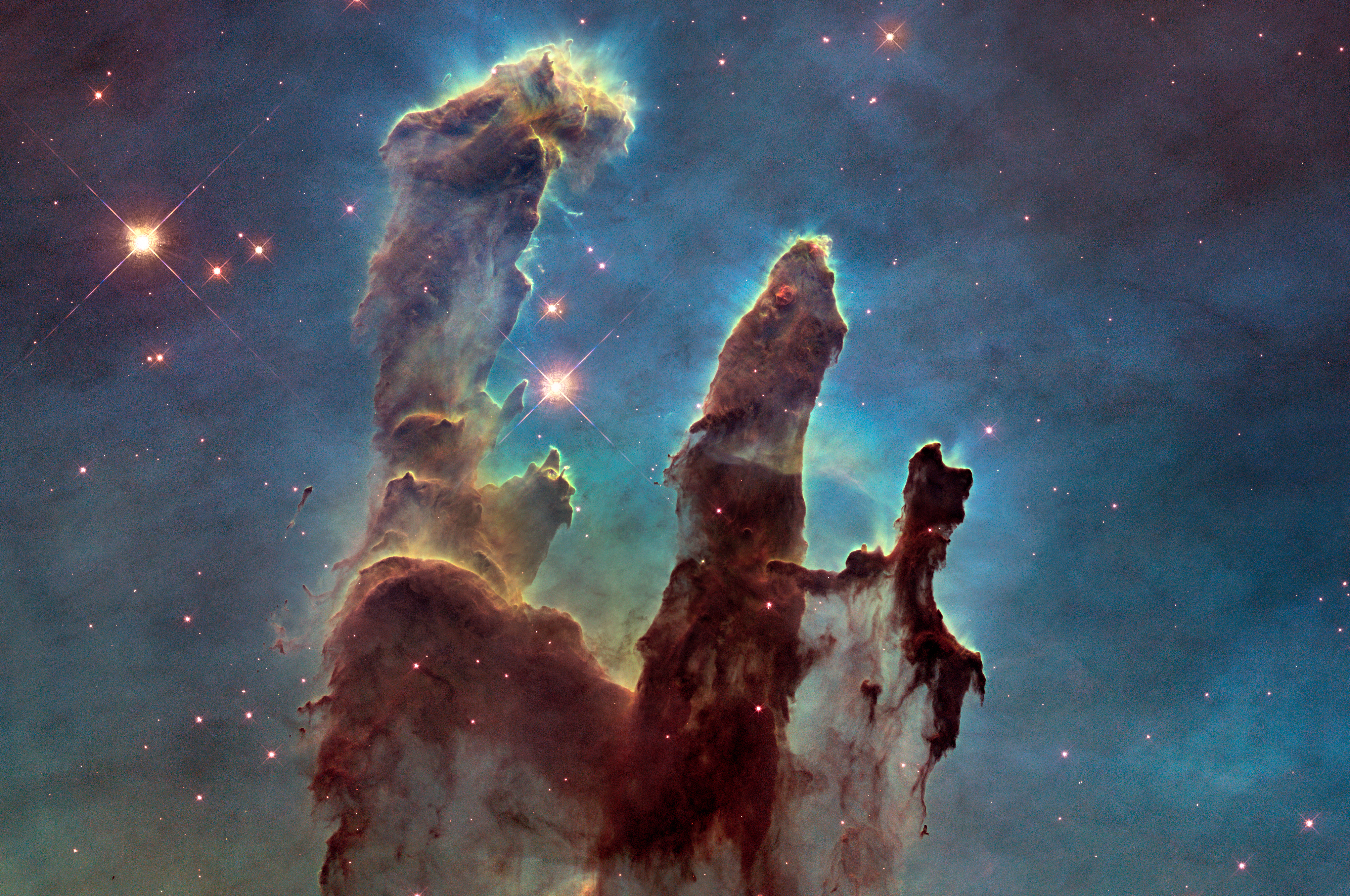 Three tall pillars of red, blue and green gas appear in space against a background of stars.