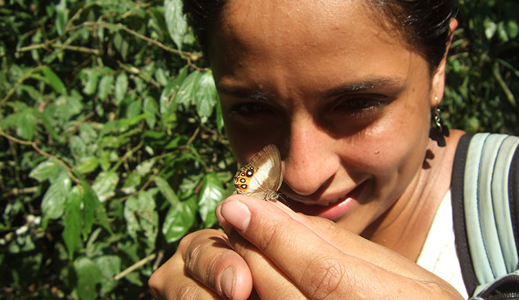 Blanca Huertas holding a small brown, orange and white butterfly during fieldwork in Peru. 