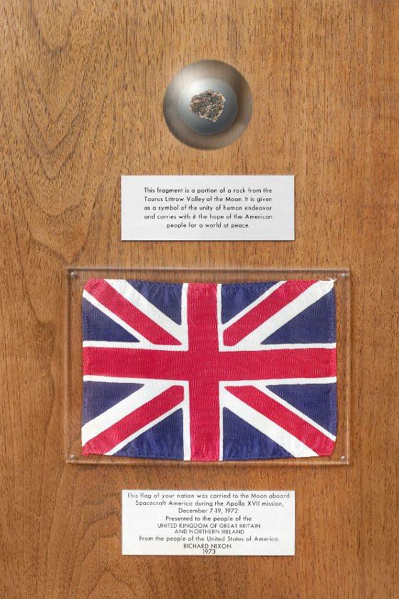 A small piece of Moon rock mounted on a wooden plaque with a union jack and two information labels