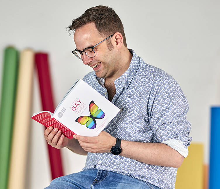 Author Josh Davis poses in the studio with his book, A Little Gay Natural History
