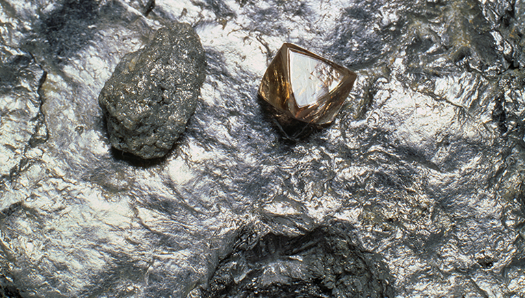 A rough diamond and a diamond crytsal. They are sitting on a base of graphite.